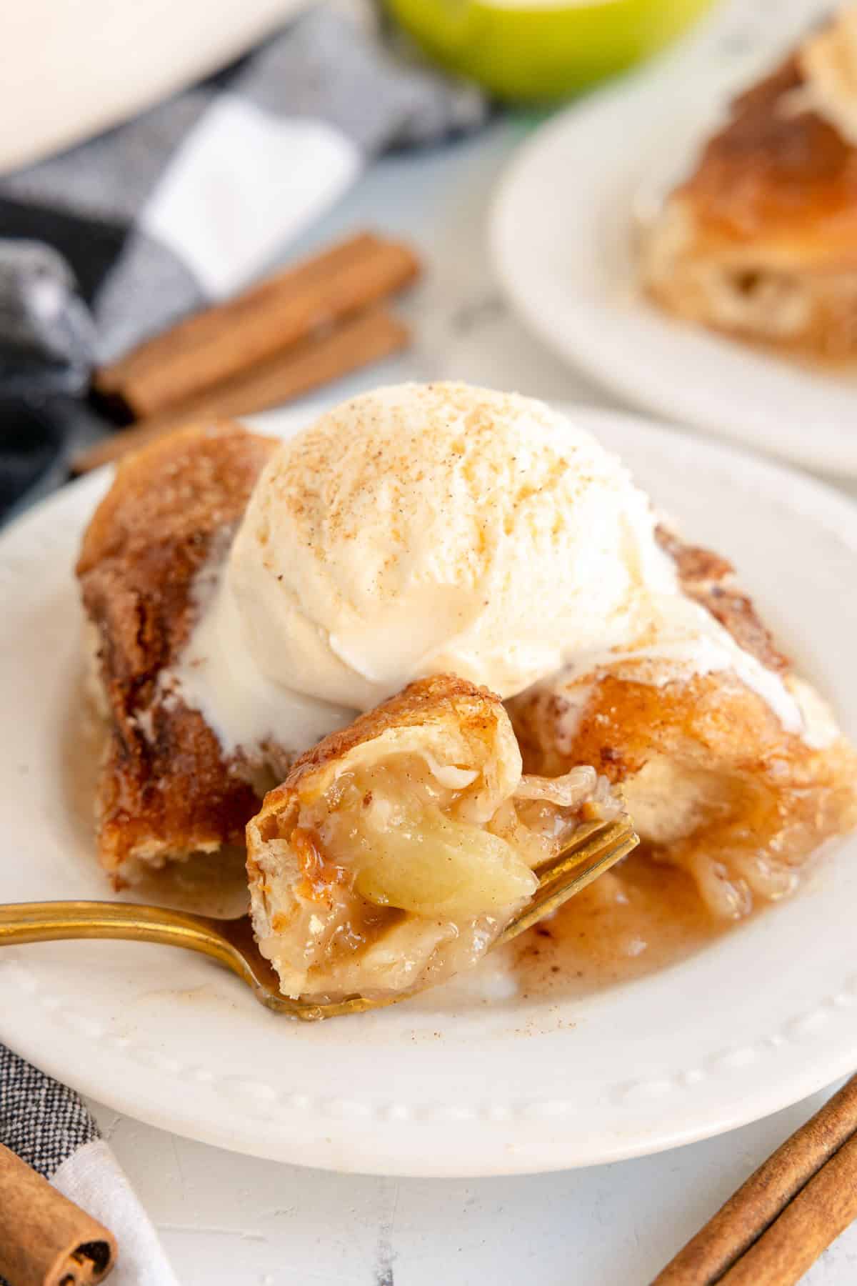 Apple dumplings topped with a scoop of vanilla ice cream on a white plate.