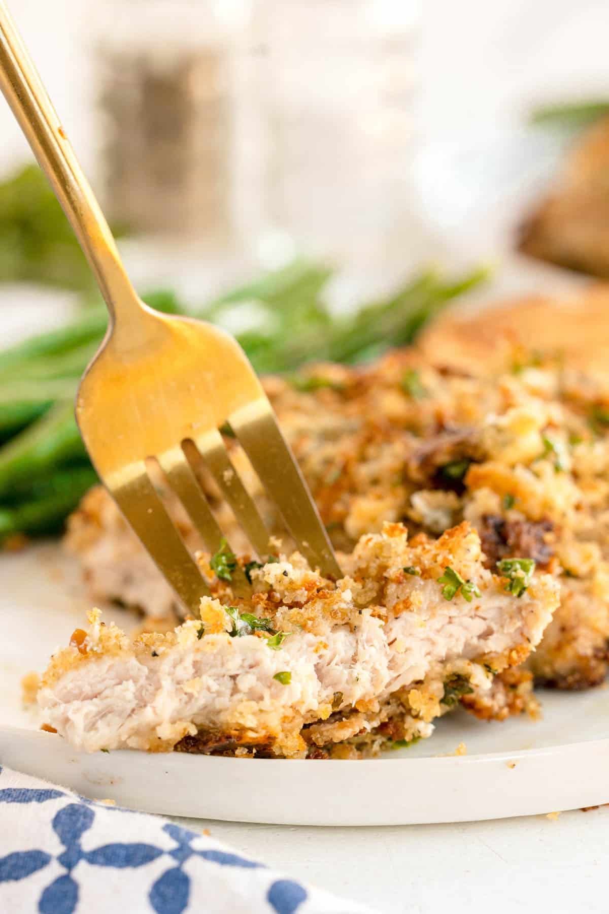 A close-up of a bite of crusted pork chop on a fork, showing the juicy inside.