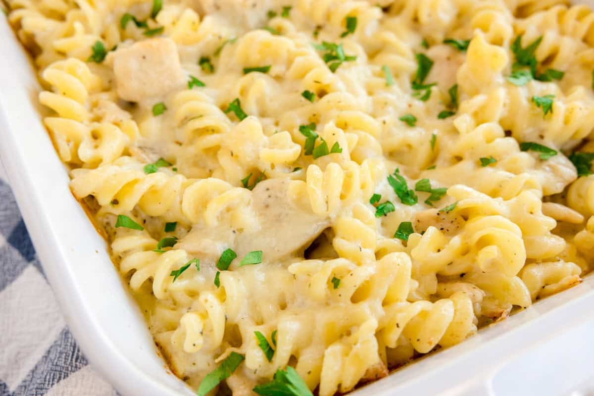 Baked rotini pasta with chicken and melted cheese, topped with chopped parsley in a white dish.