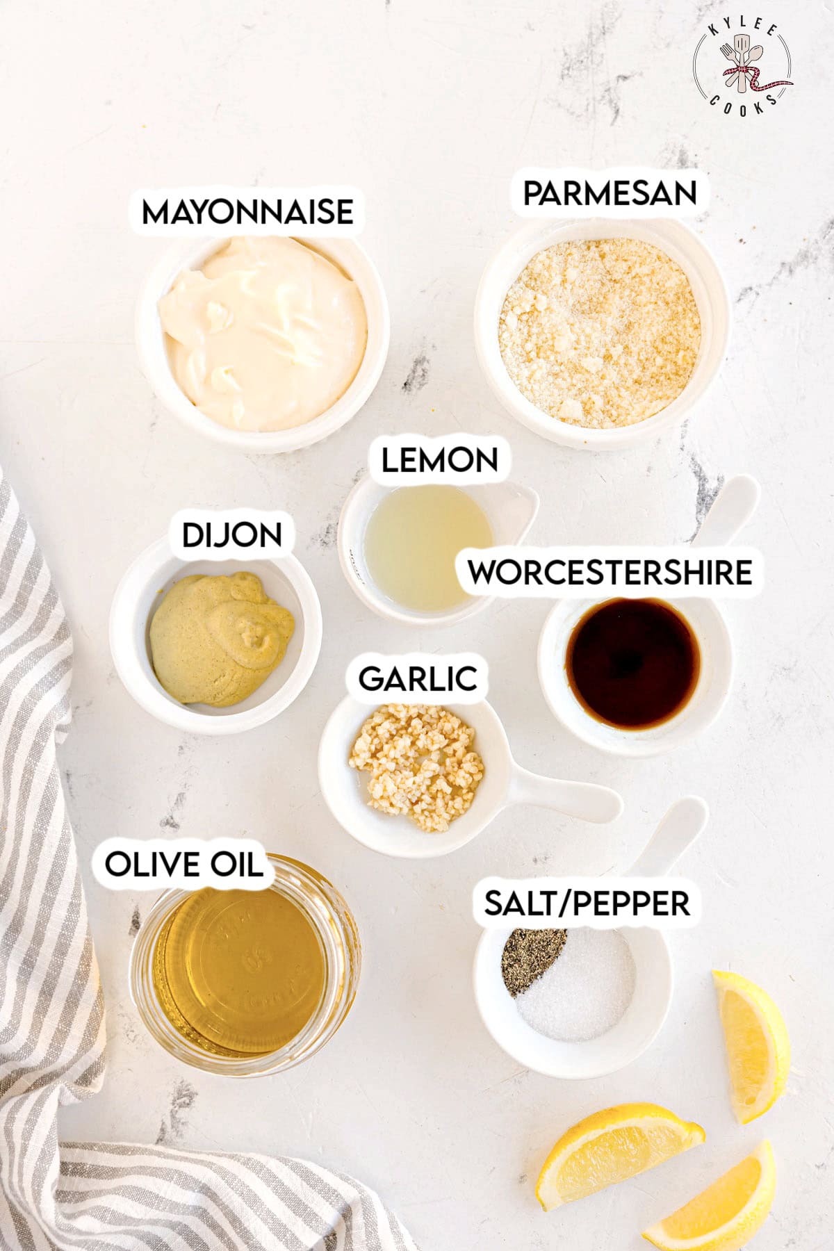 Small bowls with mayonnaise, parmesan, lemon juice, Dijon, Worcestershire, garlic, olive oil, and salt/pepper arranged on a white surface. Text on the image says 'MAYONNAISE', 'PARMESAN', 'LEMON', 'DIJON', 'WORCESTERSHIRE', 'GARLIC', 'OLIVE OIL', 'SALT/PEPPER'.