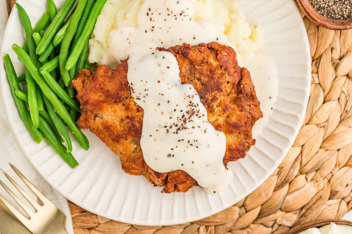 Overhead view of chicken fried steak with gravy, mashed potatoes, and green beans.