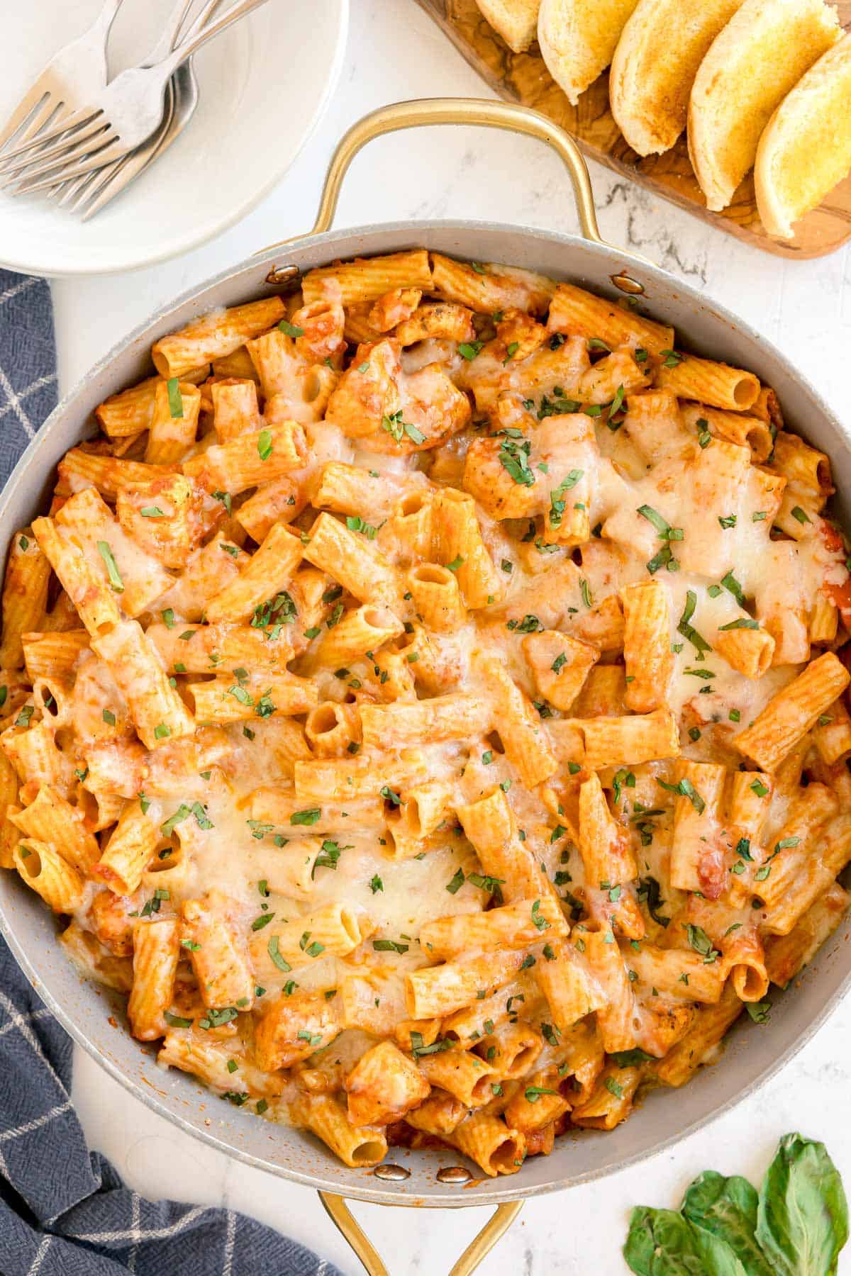 A pan of baked rigatoni with chicken, marinara sauce, melted cheese, and chopped basil.