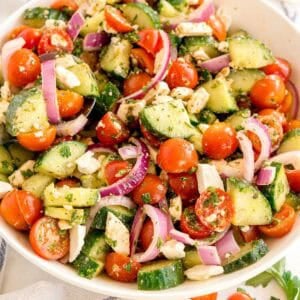 A bowl filled with chopped cucumber, cherry tomatoes, red onion, parsley, and feta cheese.