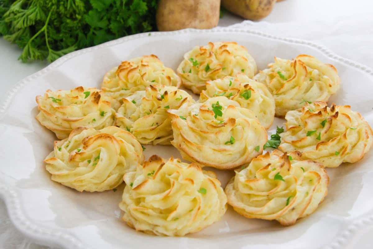 A white platter with duchess potatoes, garnished with parsley.