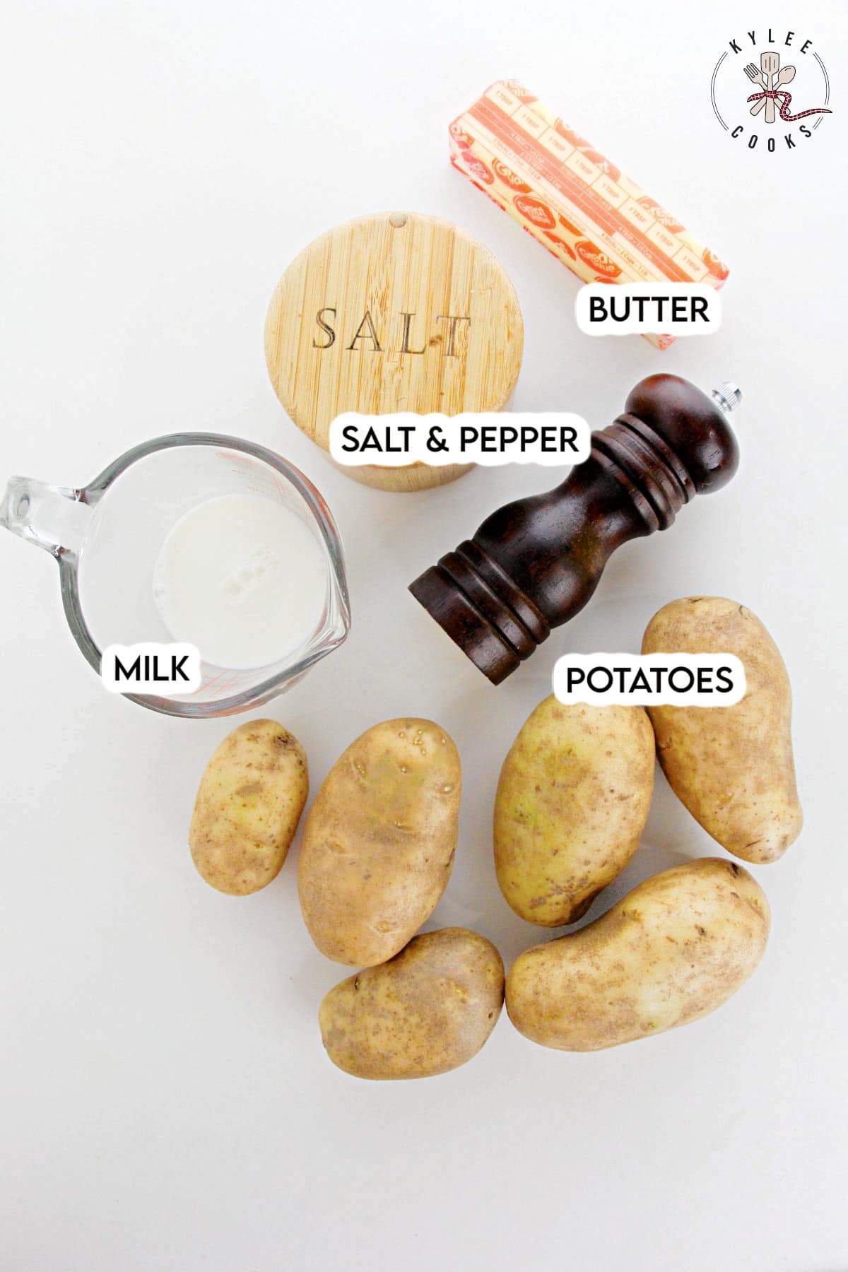 Potatoes, a stick of butter, a glass measuring cup with milk, salt, and a pepper grinder. Text on the image says 'BUTTER', 'SALT & PEPPER', 'MILK', 'POTATOES'.