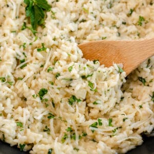 A close-up of creamy risotto mixed with chopped herbs, being stirred with a wooden spoon.