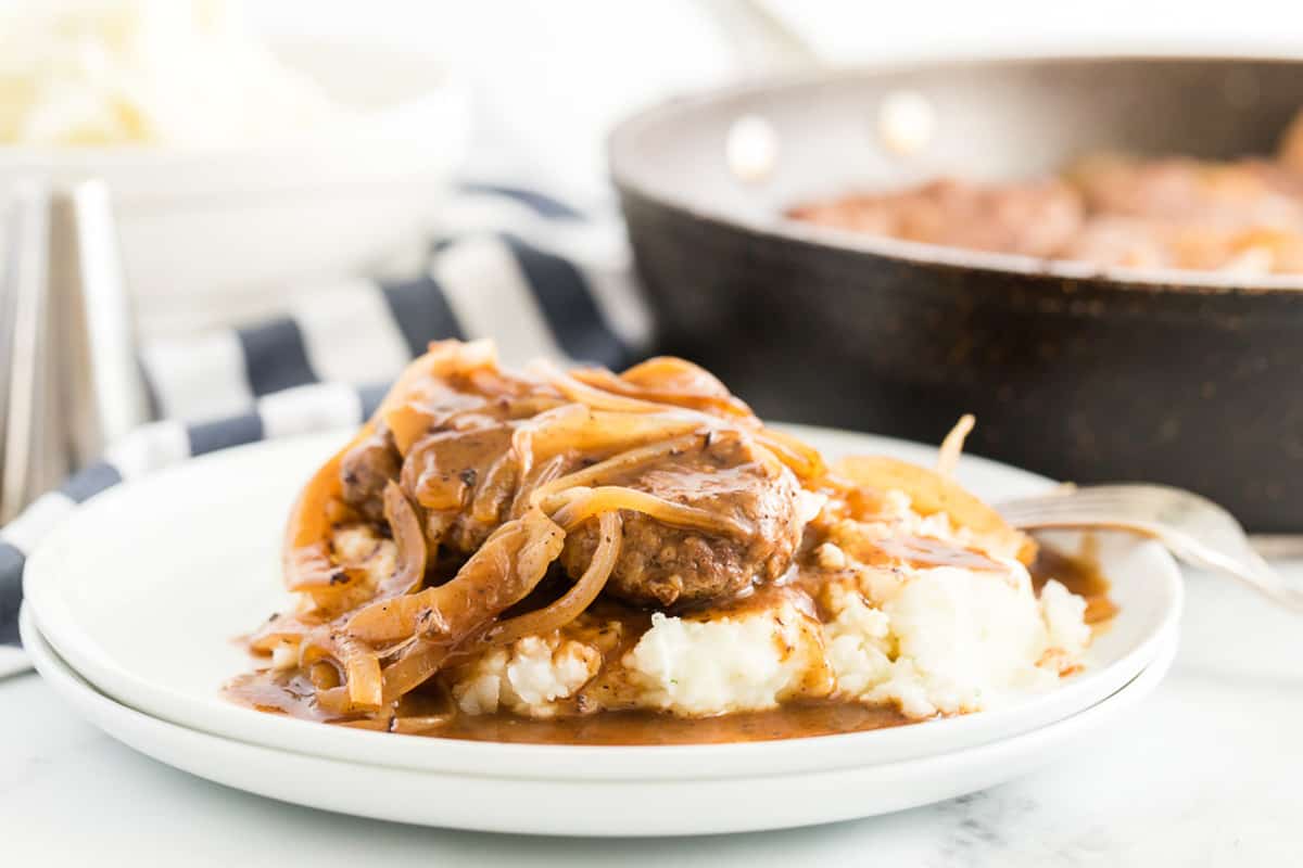 hamburger steaks on a white plate smothered in onions
