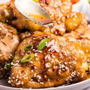 Chicken thighs topped with sesame seeds and chopped green onions, with sauce being spooned over.