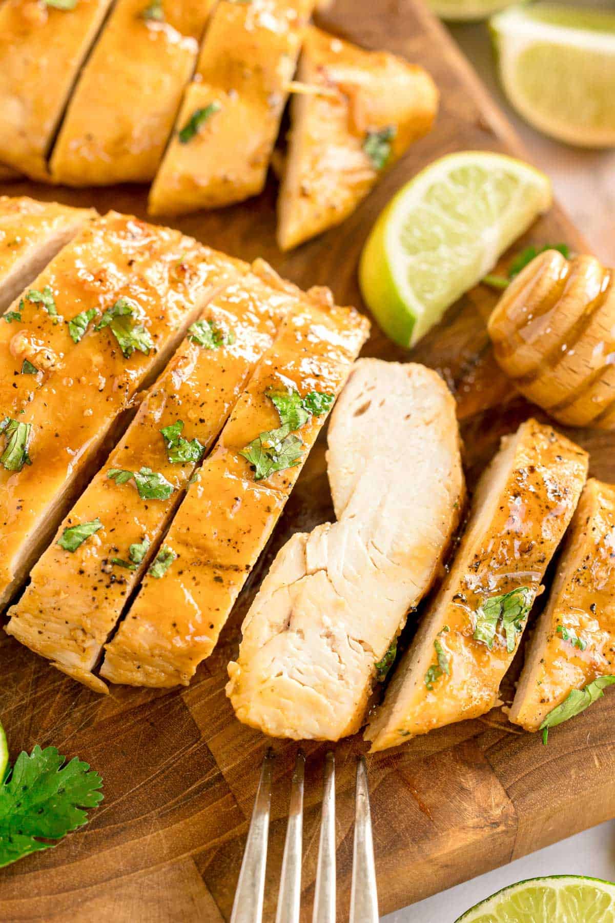 Sliced chicken breast on a cutting board with chopped cilantro and lime wedges.