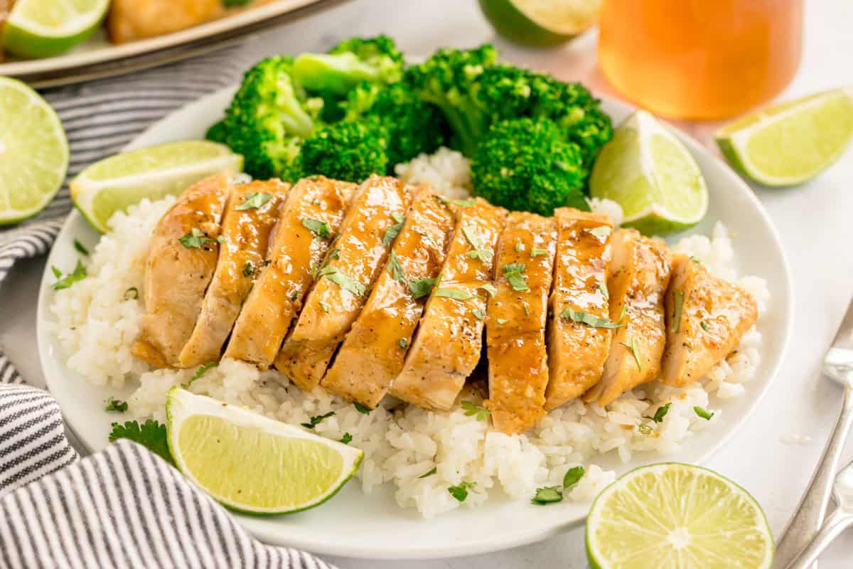 Sliced chicken breast served over rice with broccoli and lime wedges.