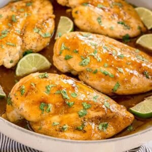 Chicken breasts in a skillet topped with sauce and chopped cilantro, with lime wedges around.