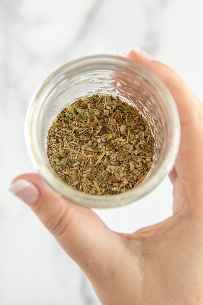 a hand holding a glass jar with italian seasoning