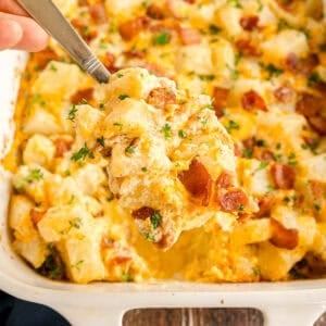 A spoonful of cheesy baked potato casserole with bacon and herbs lifted from a baking dish.