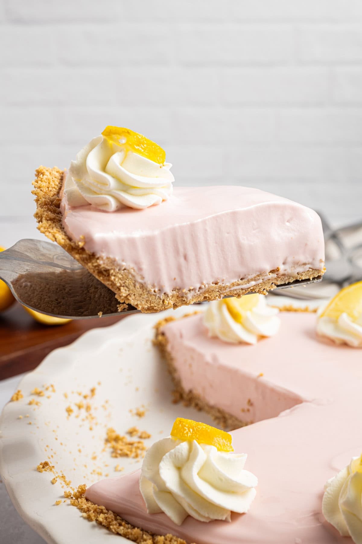 A slice of pink lemonade pie on a white plate with a crumbly crust and whipped cream topping.