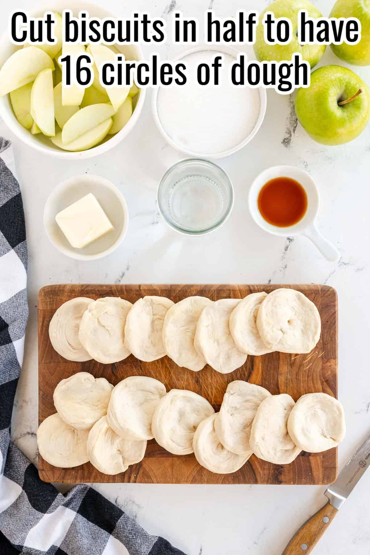 Sliced biscuit dough arranged on a wooden board surrounded by bowls containing apple slices, sugar, butter, and a small container of liquid. Text above reads, "Cut biscuits in half to have 16 circles of dough.