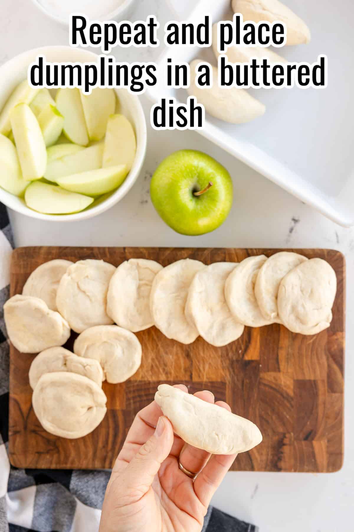 A hand holding a piece of dough, with several pieces of dough on a wooden cutting board, apple slices in a bowl, a green apple, and a buttered dish in the background. Text reads: "Repeat and place dumplings in a buttered dish".