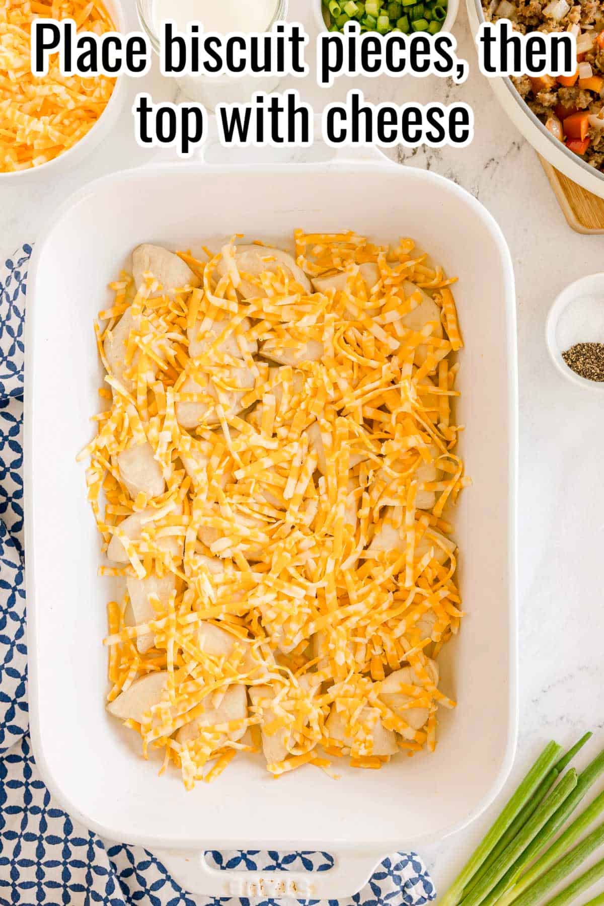 Biscuit dough pieces in a baking dish topped with shredded cheese. Text on the image says 'Place biscuit pieces, then top with cheese'.