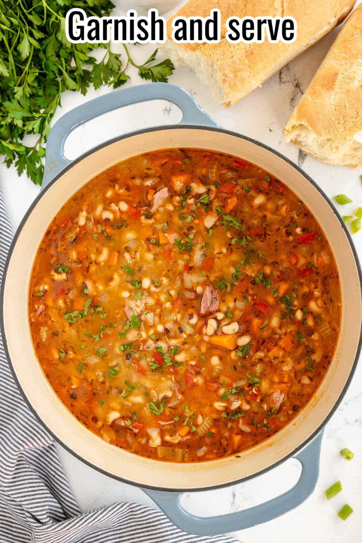 A pot of hearty black-eyed pea and vegetable soup with herbs, accompanied by sliced bread and a parsley garnish.
