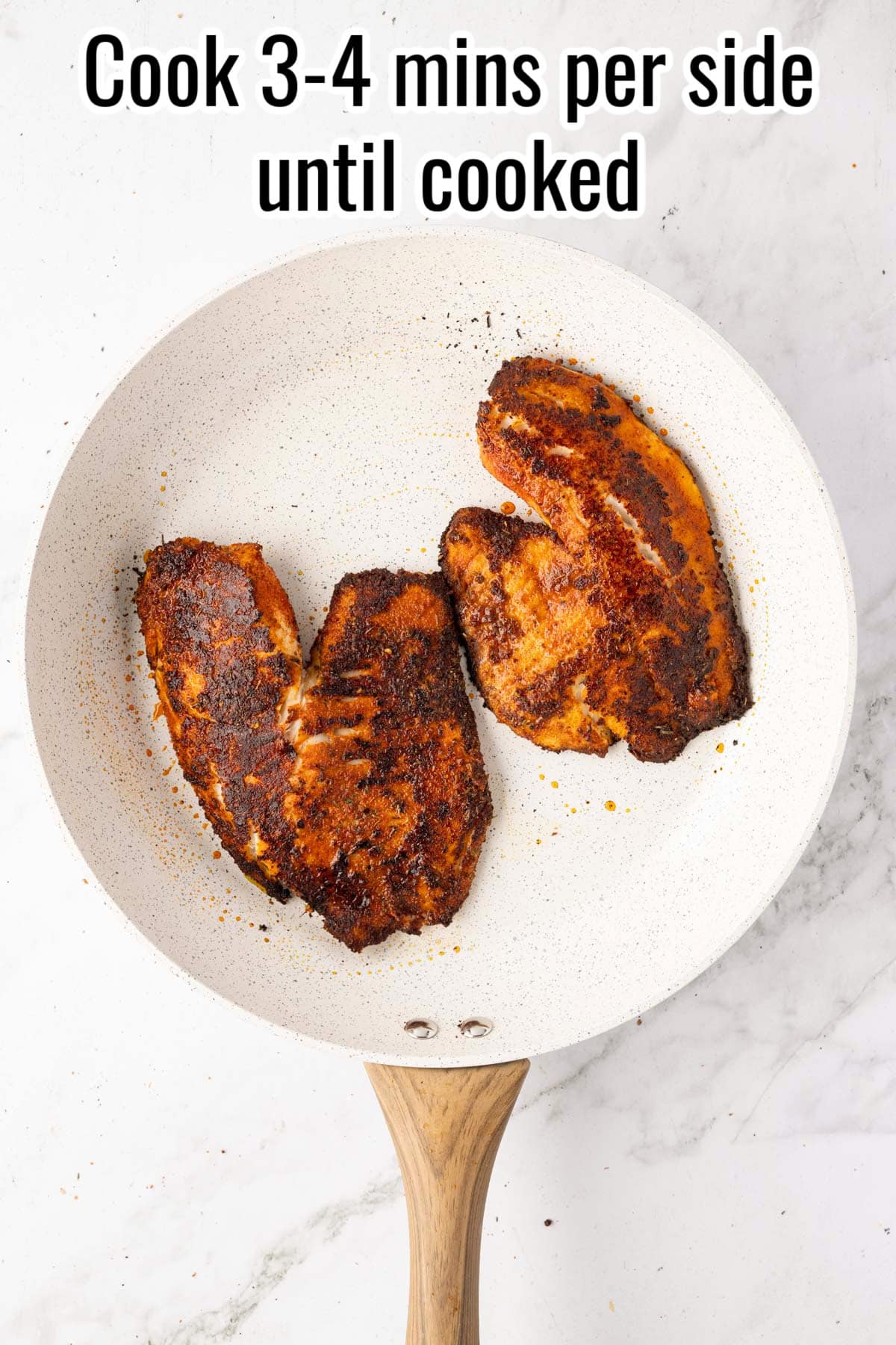 Cooked blackened tilapia in a skillet. Text on the image says 'Cook 3-4 mins per side until cooked'.