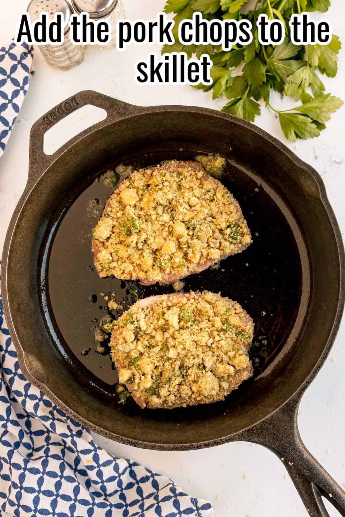 Two pork chops with crumb topping in a cast iron skillet. Text on the image says 'Add the pork chops to the skillet'.