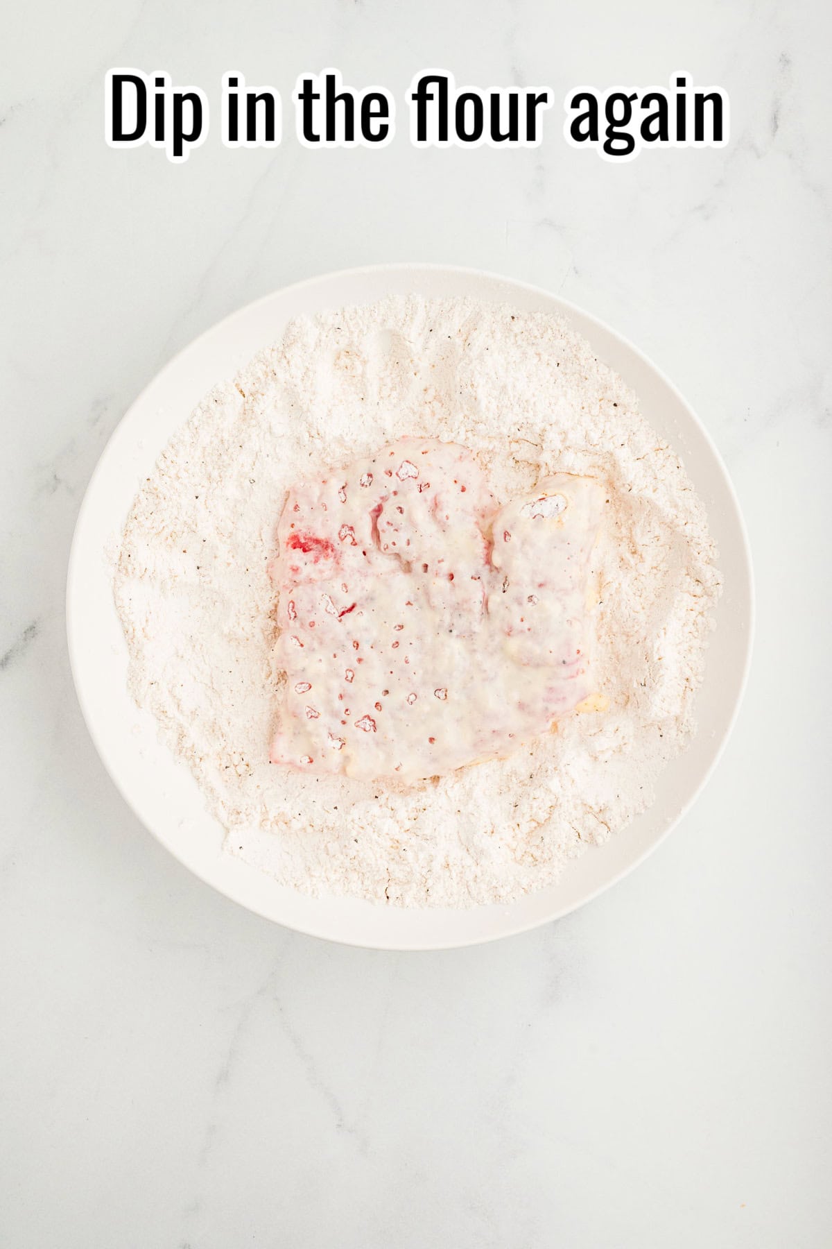 Cube steak coated in wet batter placed in a bowl of flour. Text on the image says 'Dip in the flour again'.