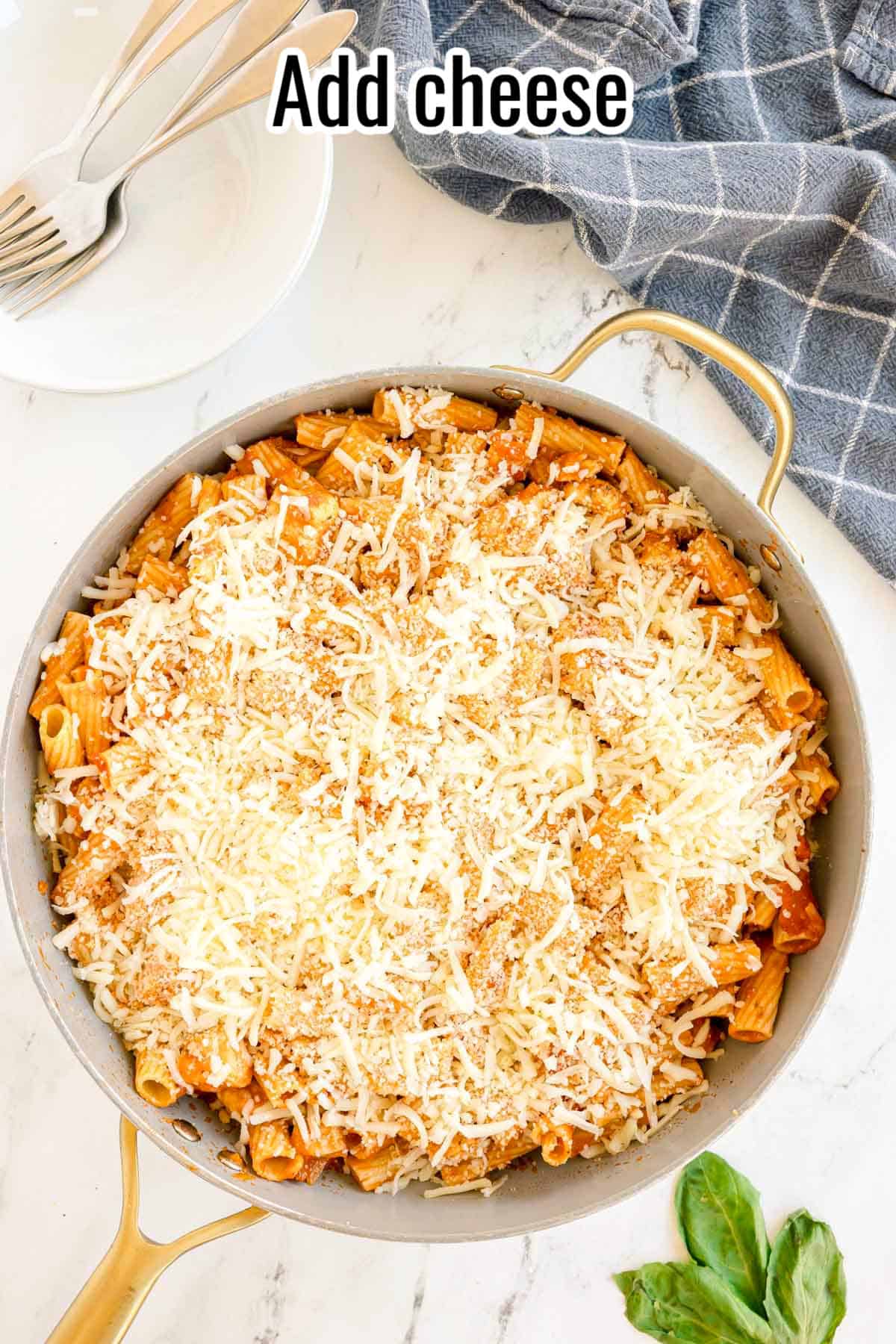 A skillet of pasta topped with shredded mozzarella and Parmesan cheese. Text on the image says 'Add cheese'.