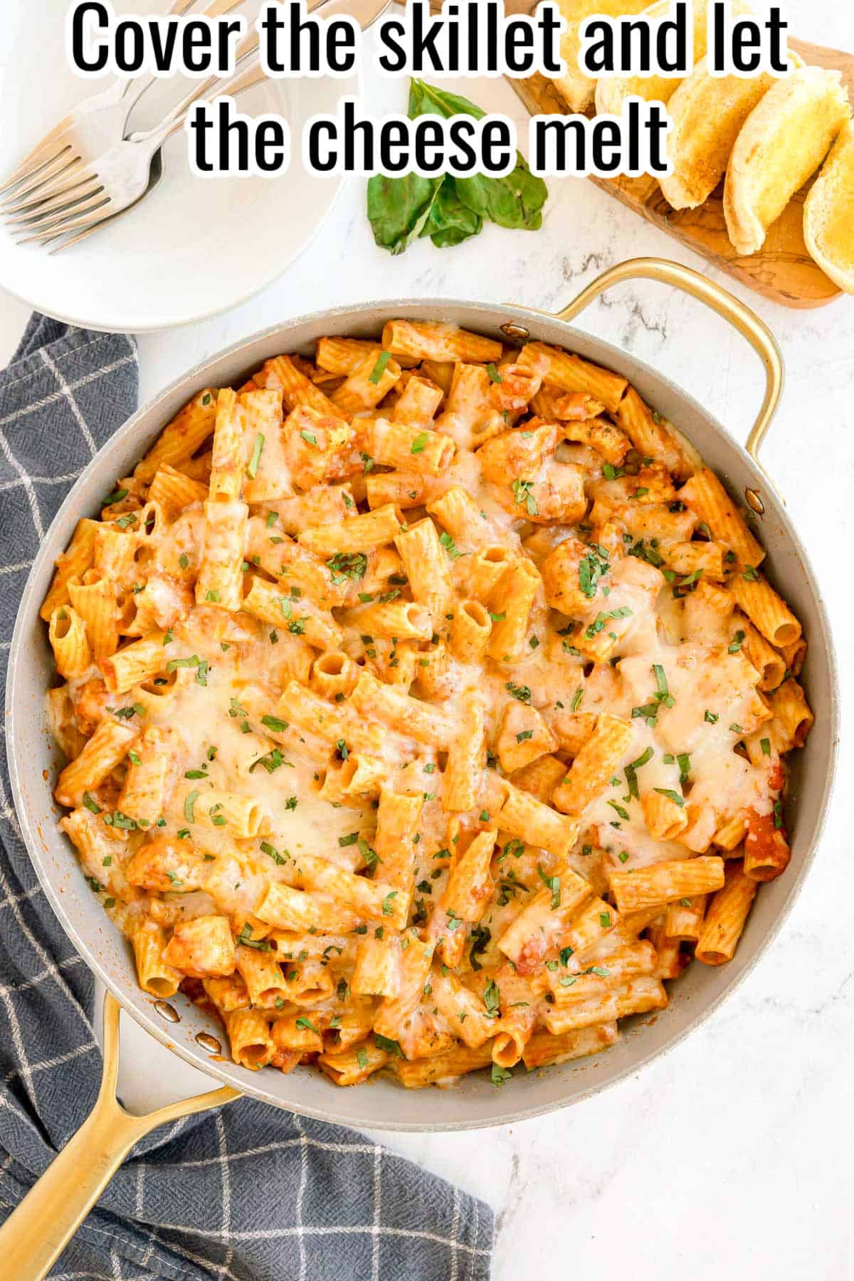 A skillet of baked rigatoni with chicken, marinara sauce, melted cheese, and basil. Text on the image says 'Cover the skillet and let the cheese melt'.