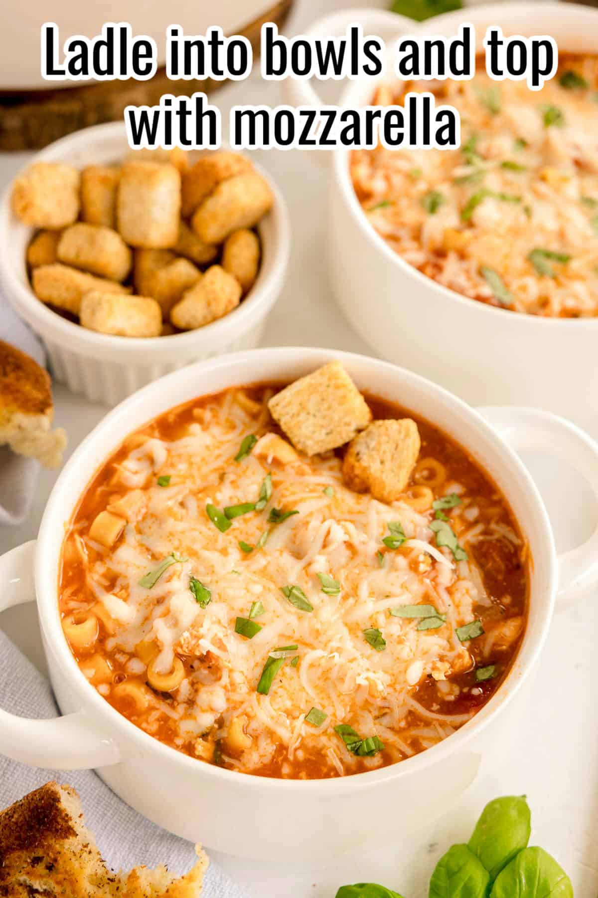 Bowls of chicken parmesan soup topped with melted mozzarella and croutons. Text on the image says 'Ladle into bowls and top with mozzarella'.