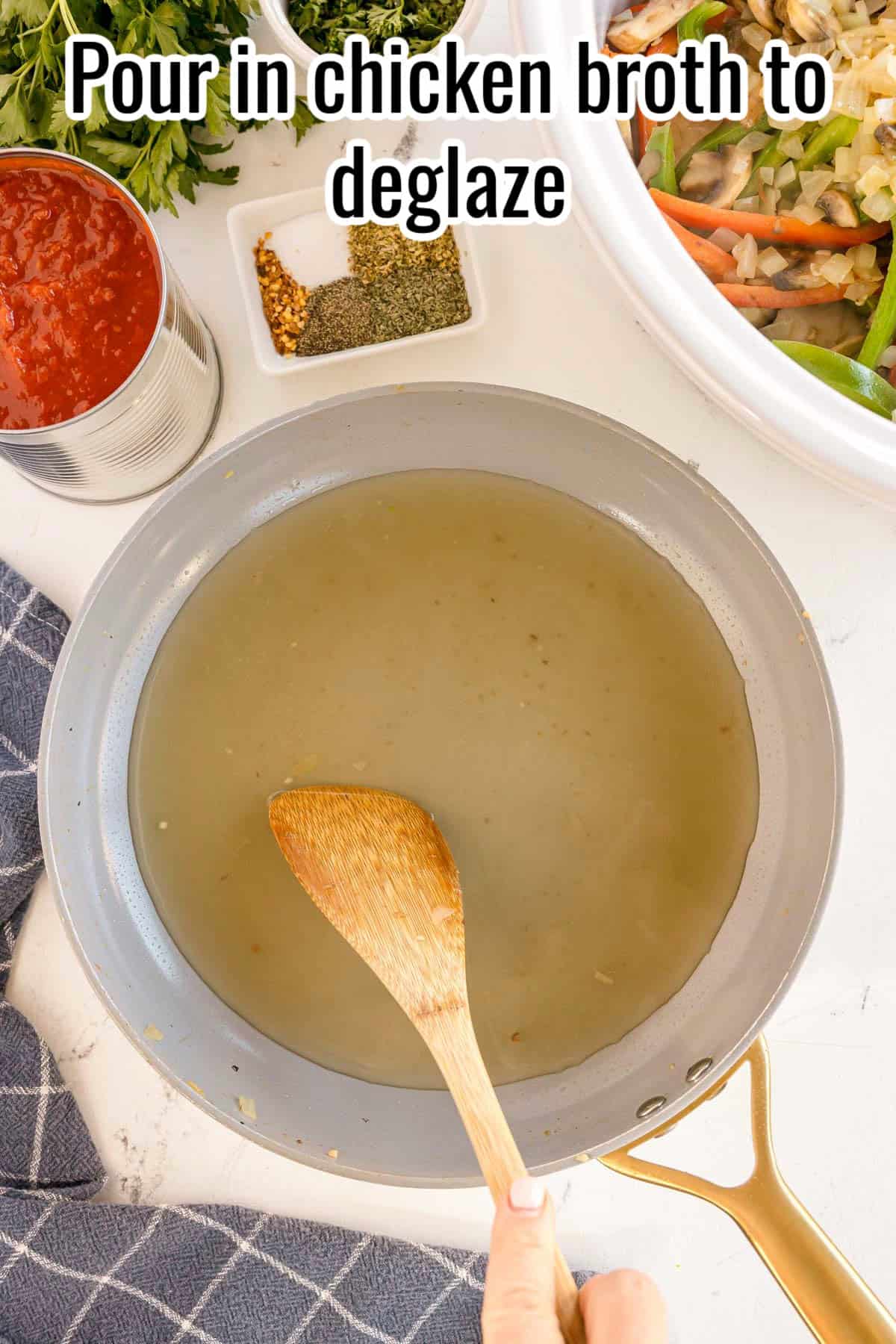 A wooden spoon stirring chicken broth in a skillet to deglaze, with a text overlay that reads "Pour in chicken broth to deglaze."