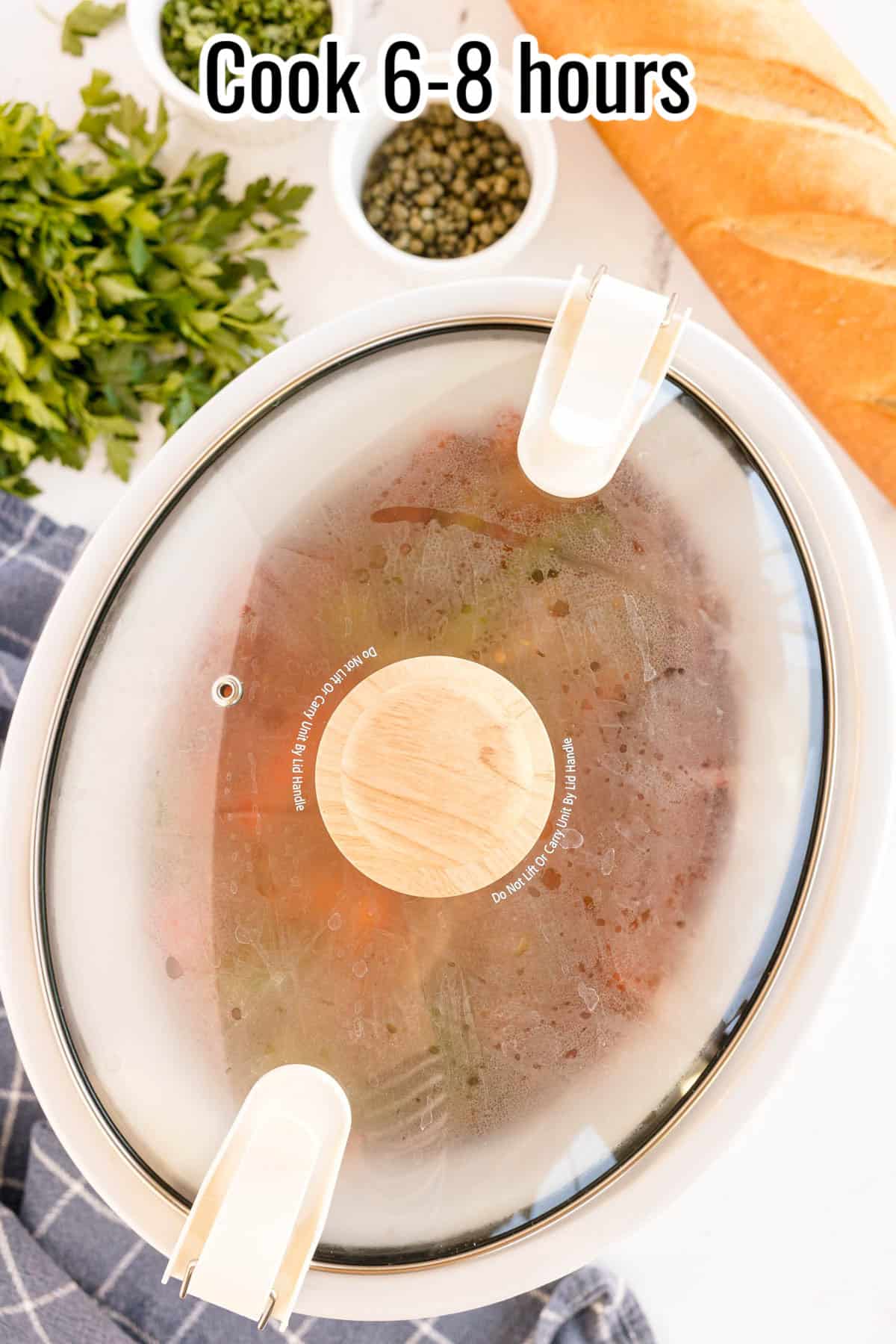 A crockpot covered with a glass lid, showing condensation as the dish cooks, with a text overlay that reads "Cook 6-8 hours."
