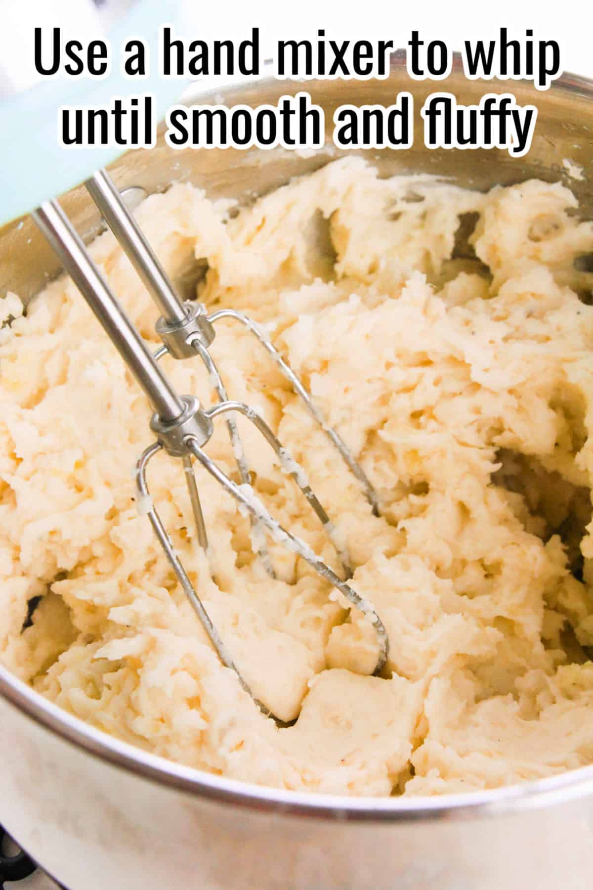 Mashed potatoes in a pot being whipped with a hand mixer. Text on the image says 'Use a hand mixer to whip until smooth and fluffy'.