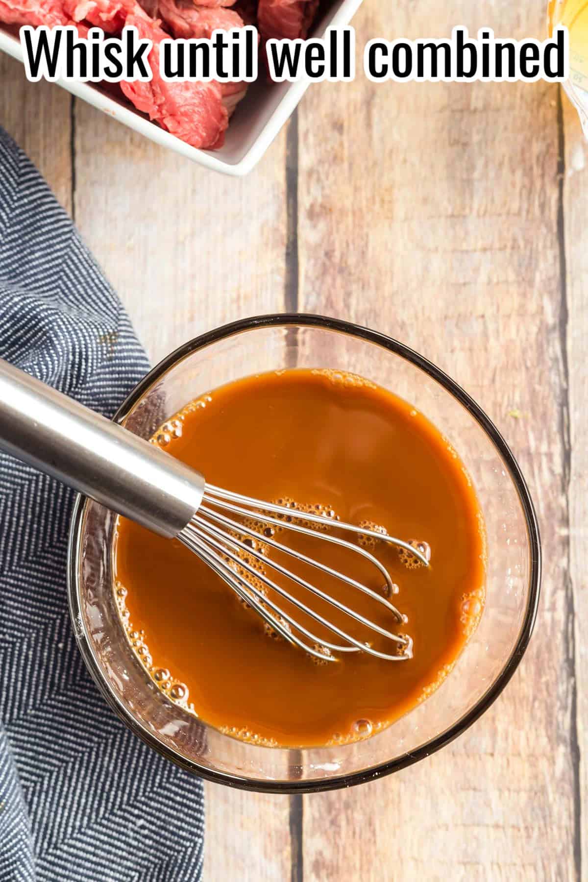A whisk stirring a glass bowl of honey soy sauce mixture until smooth. Text on the image says 'Whisk until well combined'.