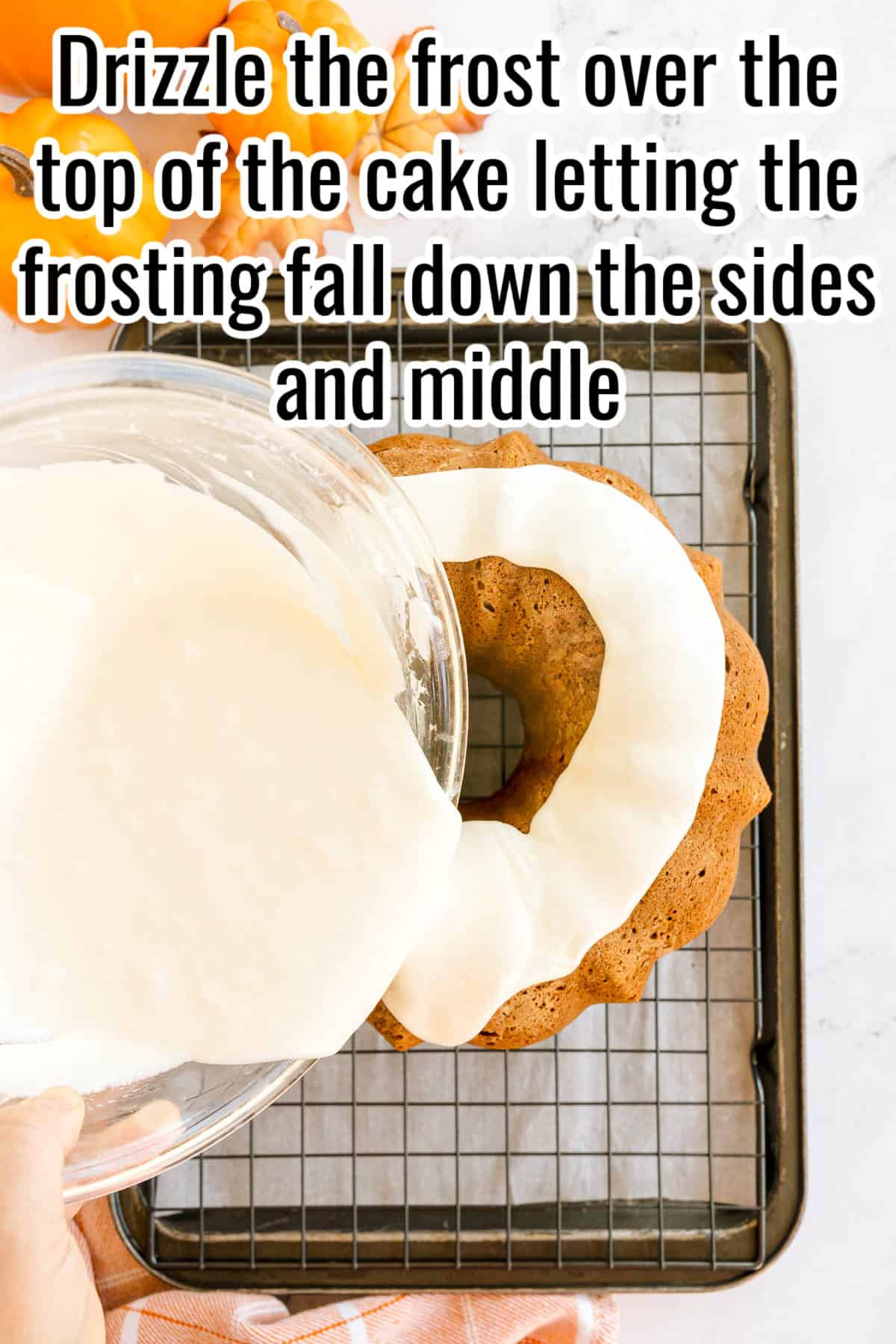 A pumpkin Bundt cake being drizzled with white frosting from a glass bowl. Text on the image says 'Drizzle the frost over the top of the cake letting the frosting fall down the sides and middle'.