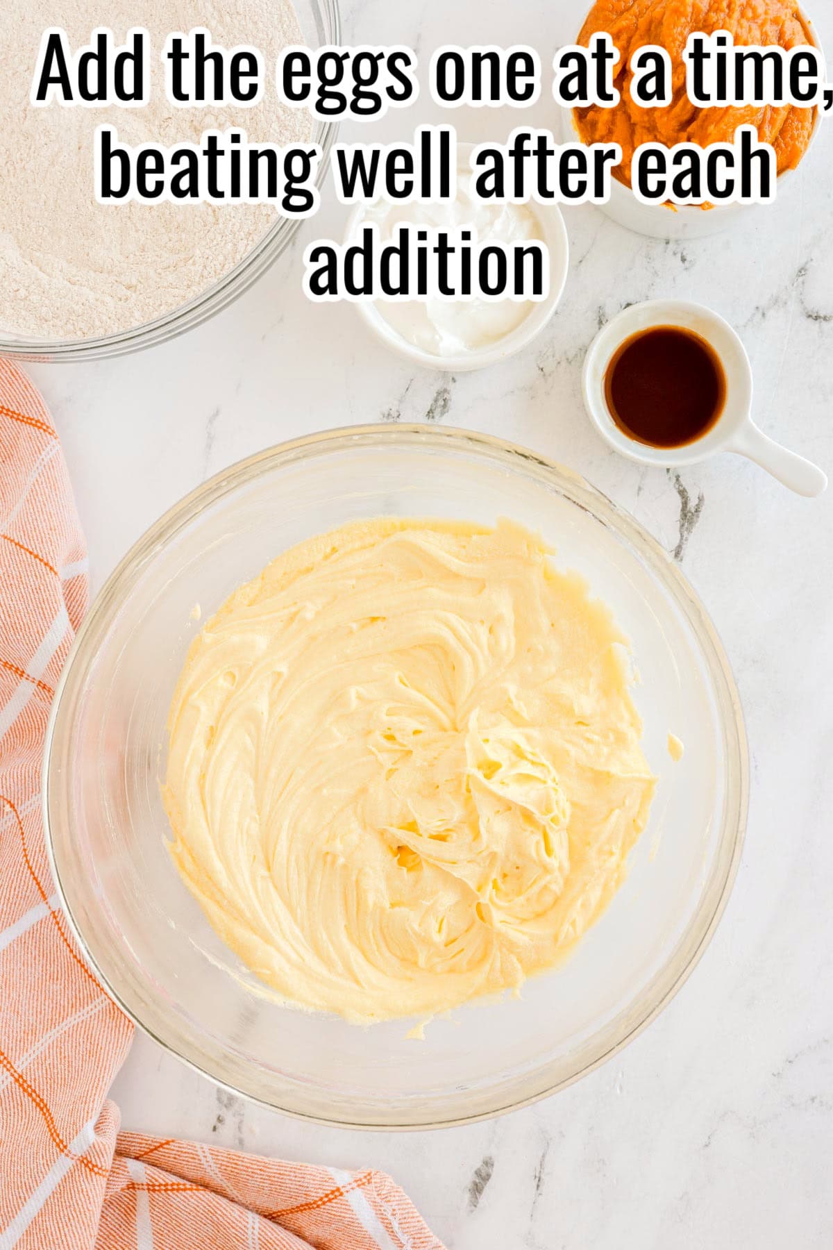 A stand mixer bowl with batter and cracked eggs. Text on the image says 'Add eggs one at a time, beating after each addition'.