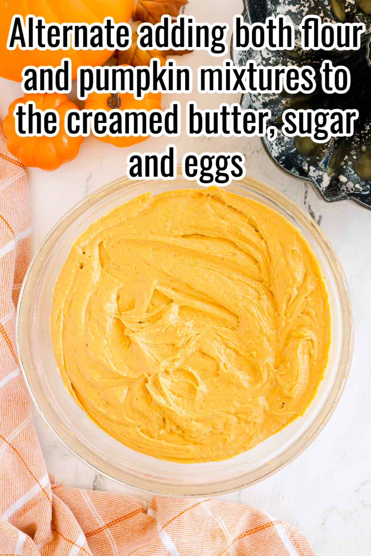 A glass mixing bowl filled with orange pumpkin cake batter. Text on the image says 'Alternate adding both flour and pumpkin mixtures to the creamed butter, sugar and eggs'.