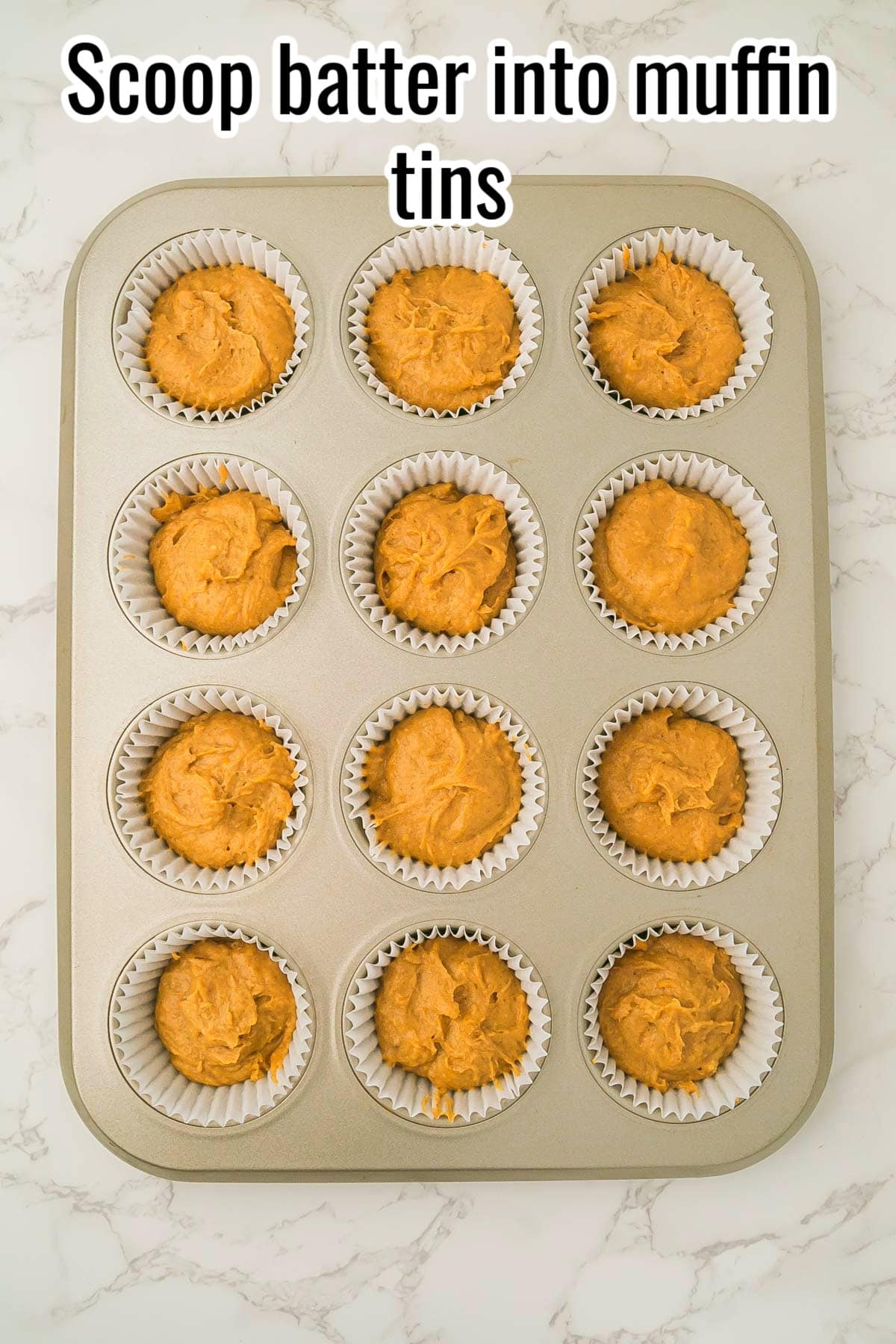 Muffin tin filled with pumpkin batter in paper liners. Text on the image says 'Scoop batter into muffin tins'.