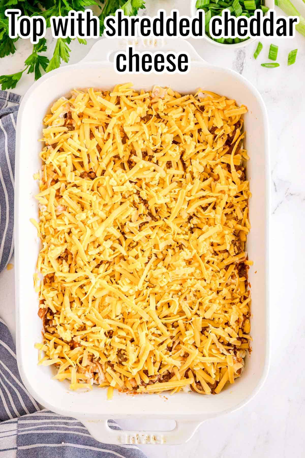 Unbaked casserole topped with shredded cheddar cheese. Text on the image says 'Top with shredded cheddar cheese'