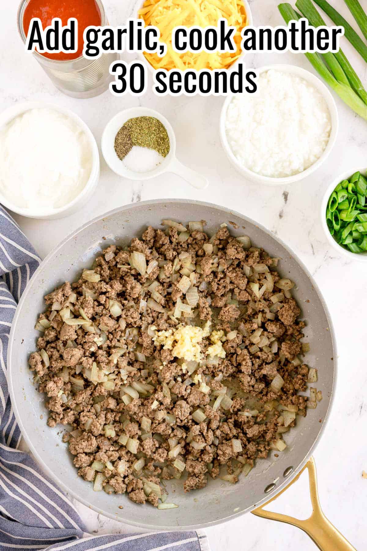 A skillet with cooked beef and onions, garlic just added. Text on the image says 'Add garlic, cook another 30 seconds'