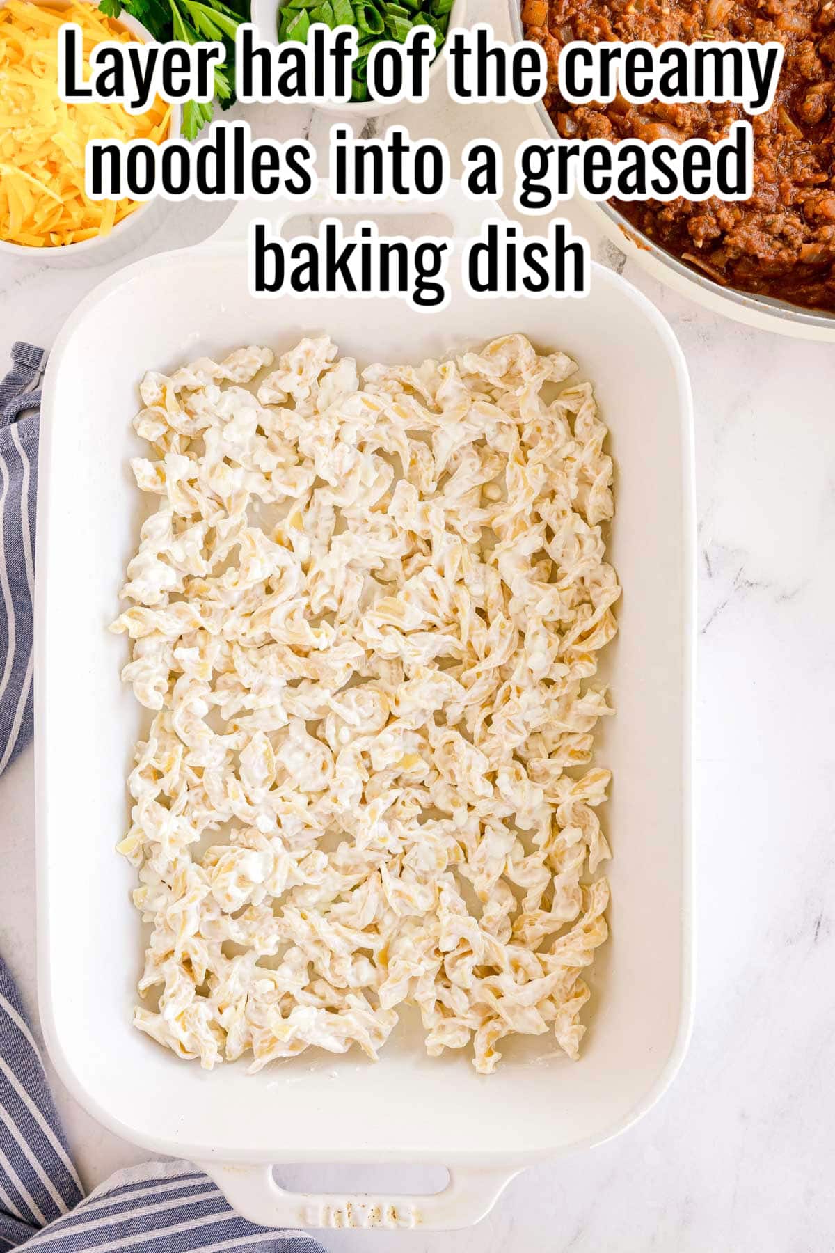 Creamy noodles spread in a baking dish. Text on the image says 'Layer half of the creamy noodles into a greased baking dish'