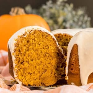A close-up of pumpkin bundt cake with cream cheese glaze, missing one slice.