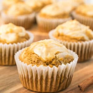 Close-up of a pumpkin cream cheese muffin in a white liner on a wooden board.