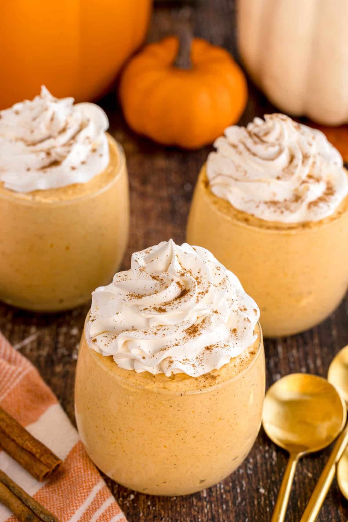 Three glasses of pumpkin mousse topped with whipped cream and cinnamon.