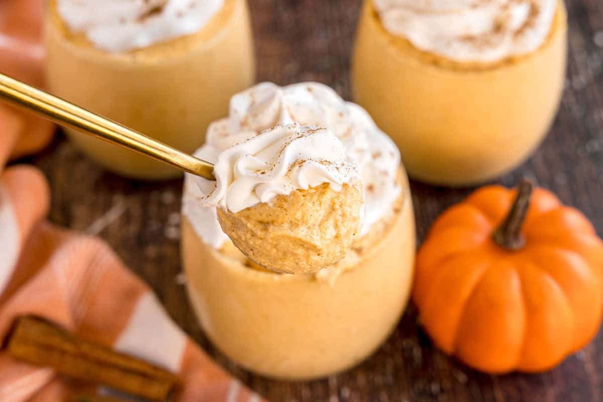 A spoonful of pumpkin mousse with whipped cream held above a glass.