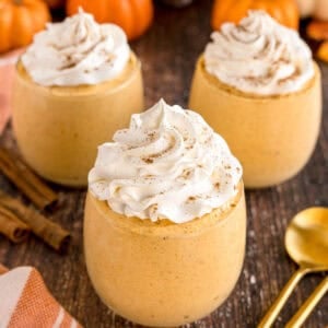 A close-up of pumpkin mousse in a glass topped with whipped cream and cinnamon.