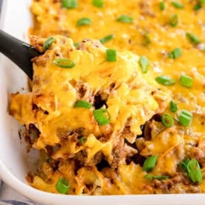 A spoonful of cheesy beef and noodle casserole being lifted from the baking dish.