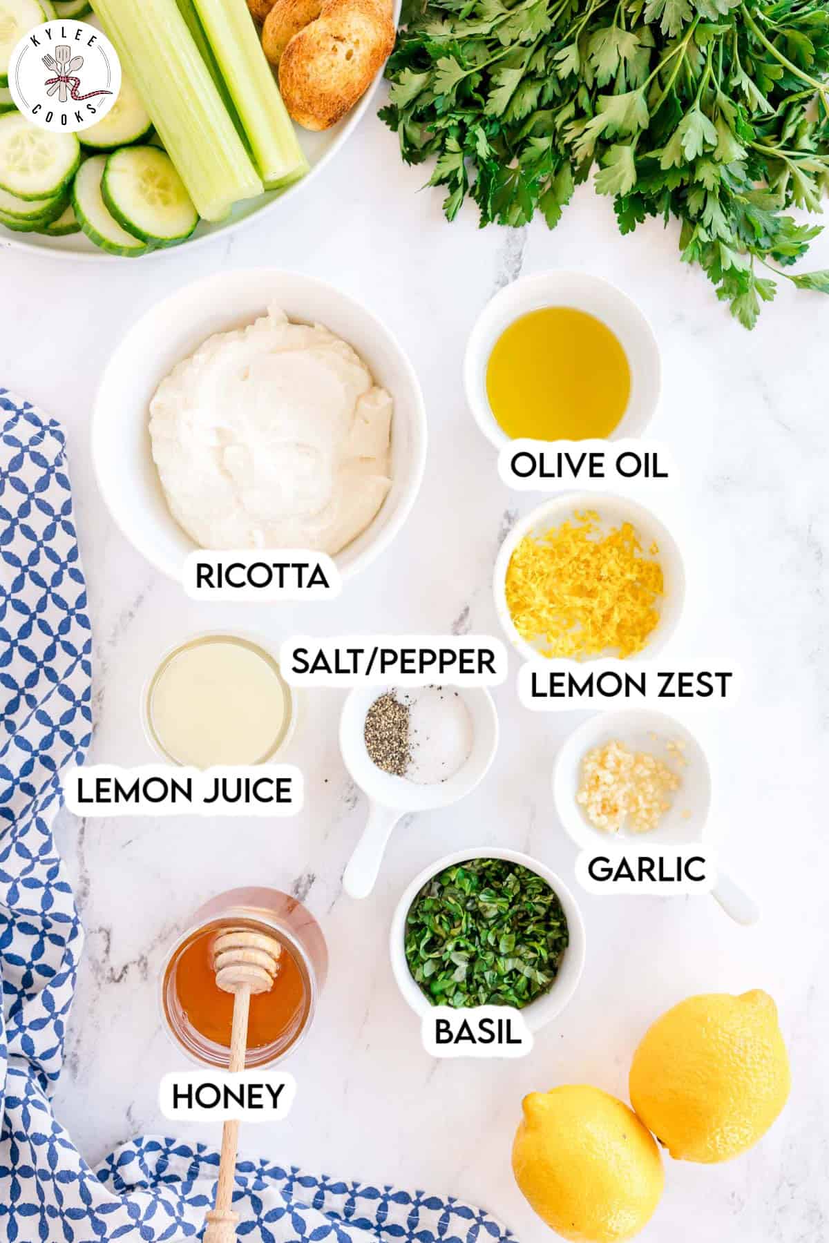 A variety of labeled ingredients for a recipe displayed on a white surface, including ricotta, olive oil, lemon zest, lemon juice, salt, pepper, garlic, basil, and honey.